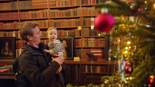 Man holding baby looking at Christmas tree in the Library at Anglesey Abbey, Cambridgeshire
